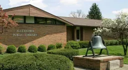 The Alexandria Public Library building on Maple Drive, with a bell mounted on the front lawn