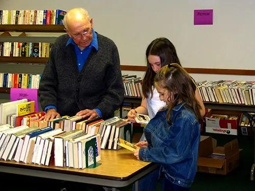 A man and a girl browsing tables of books at a library book sale