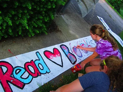 Children painting a large Read Books banner on the sidewalk outside the library