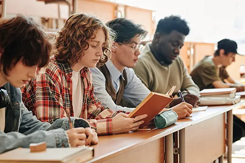 Teenage students reading books at their desks in a bright classroom